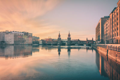 Oberbaum bridge over spree river amidst buildings at sunset