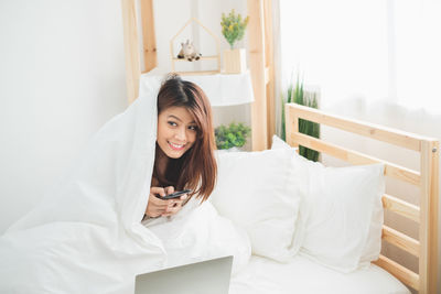 Young woman using phone while sitting on bed at home