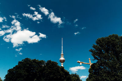 Low angle view of fernsehturm with trees and crane against sky