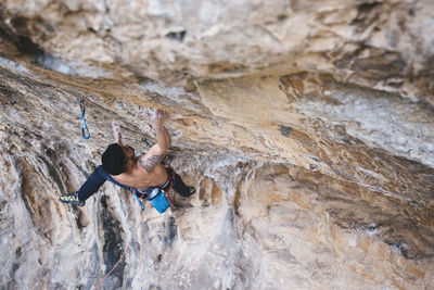 Shirtless climber sending a sport climbing route on spanish crag.