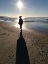 Silhouette woman standing on shore at beach against sky