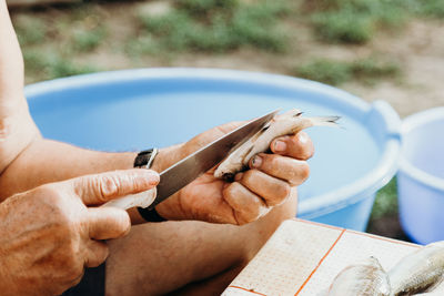 An elderly man guts fish while sitting at a table.
