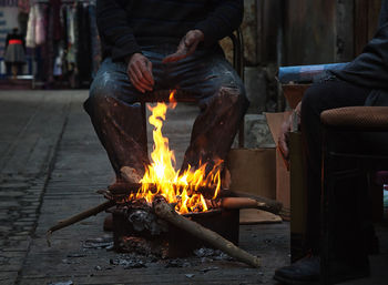 Low section of man sitting outdoors by a fire 