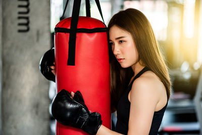 Side view of young woman holding punching bag while standing in gym