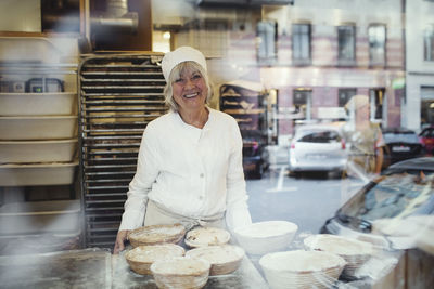 Portrait of senior smiling baker at bakery seen from glass window