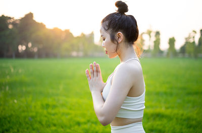 Side view of young woman drinking water against sky