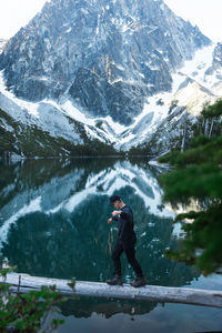 Full length of man standing on tree trunk against snowcapped mountain