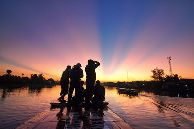 Silhouette people by swimming pool against sky during sunset