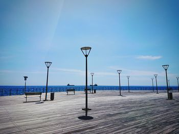 Street lights on pier by sea against blue sky