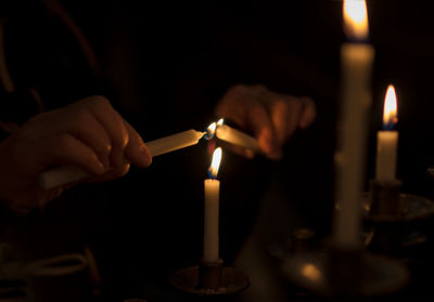 Cropped hands igniting candles in darkroom