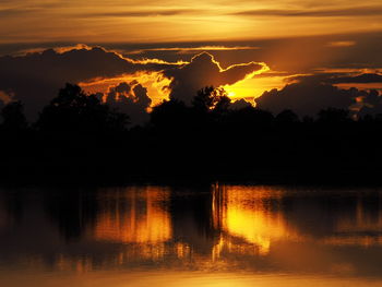 Silhouette trees by lake against orange sky