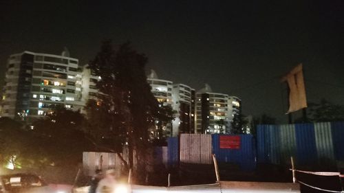 Illuminated buildings by street against sky at night