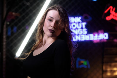 Portrait of young woman standing against illuminated nightclub