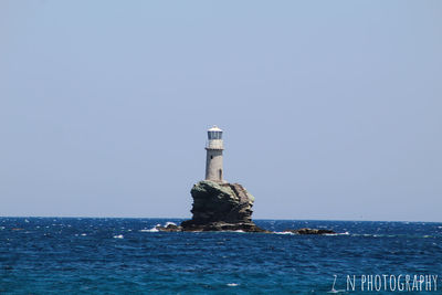 Lighthouse by sea against clear sky