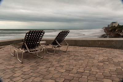 Empty chairs on beach against sky