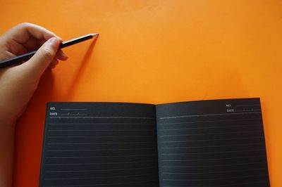 Cropped hand holding pencil by book on yellow background