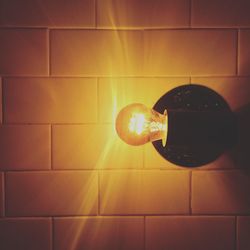 Illuminated light bulb against tiled wall