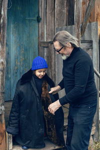 Grandson in a blue hat and boots with a grandfather in a sheepskin coat stand 