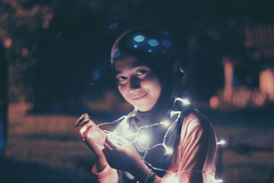 Close-up portrait of smiling girl holding illuminated lights