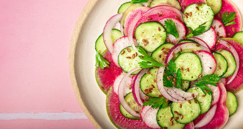 Healthy vegan salad with watermelon radish, cucumber and red onion on pink tile background.