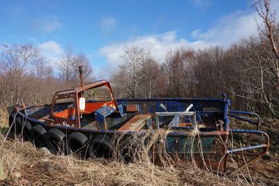 Abandoned boat on landscape against blue sky and clouds