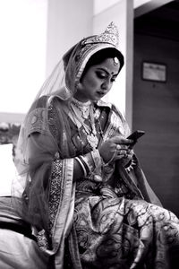 Low angle view of beautiful bride using mobile phone while sitting on bed at home