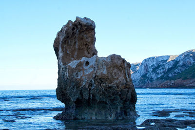 Rock formation in sea against clear blue sky