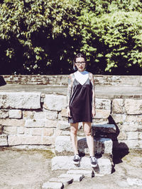 Full length portrait of young woman standing on steps on sunny day