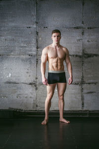 Portrait of shirtless muscular man standing by wall