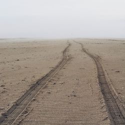 Tire track on beach against sky 