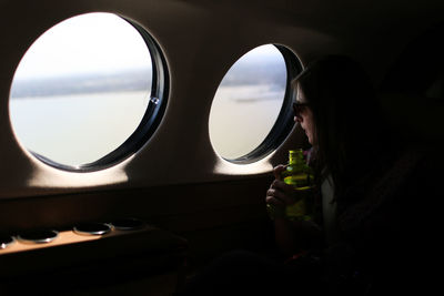 Woman looking through window while traveling in airplane