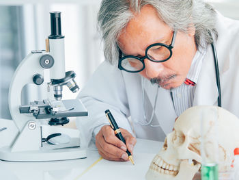Scientist examining human skull on table while sitting in laboratory