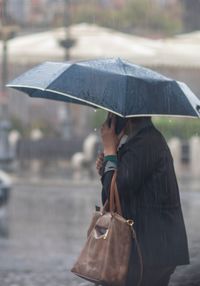 Side view of woman with umbrella walking on street during rainy season