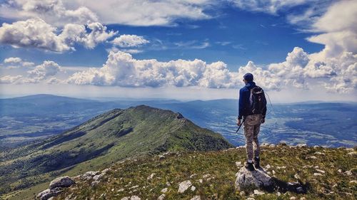 Rear view of man standing on mountain against cloudy sky