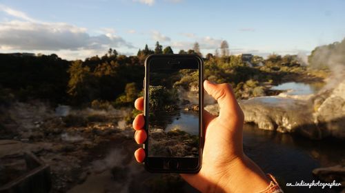 Midsection of person photographing with mobile phone against sky