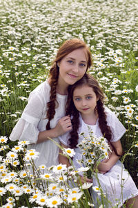 Mother with daughter in a white dress and hat stand in a daisy field in summer