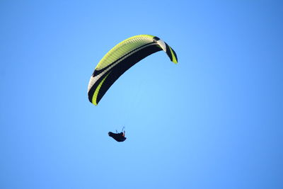 Low angle view of woman paragliding against clear blue sky