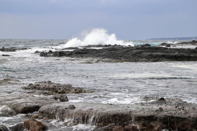 Waves splashing on rocks at shore against sky