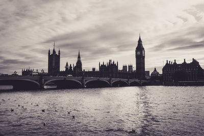 Bridge over river in city against cloudy sky