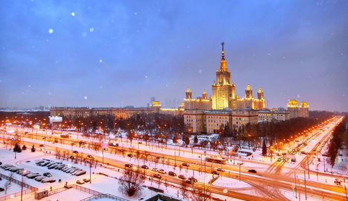 Snowfall over illuminated campus of noscow university, evening aerial view