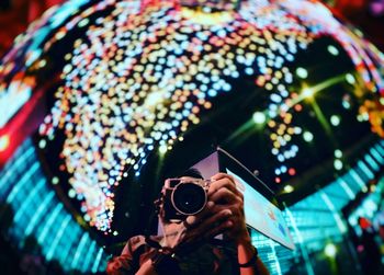 Reflection of man photographing against illuminated lighting decoration at night