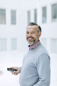 Portrait of happy businessman listening music through smart phone in office