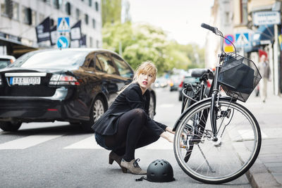 Businesswoman looking away while repairing bicycle on street