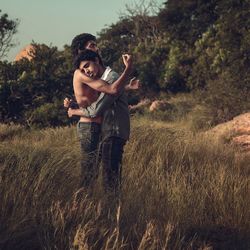 Side view of gay couple embracing on grassy field