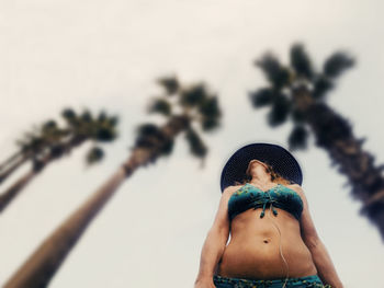 Low angle view of woman in bikini against trees and sky