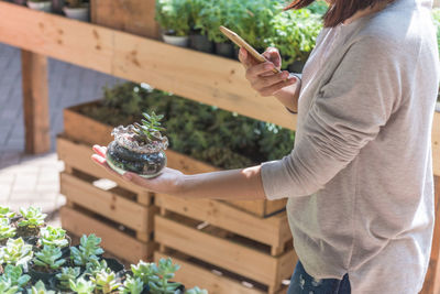 Midsection of woman holding smart phone while standing on plant