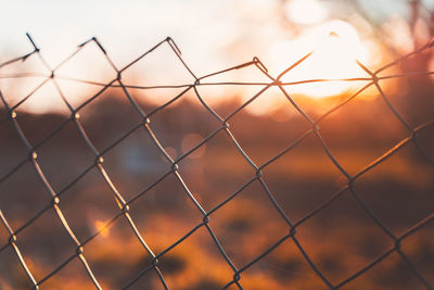 Close-up of chainlink fence against sunset sky