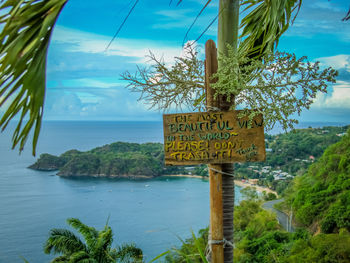 Information sign by tree by sea against sky