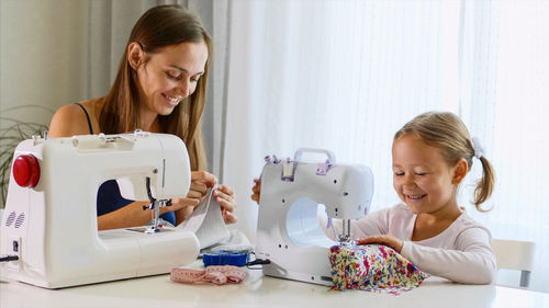 Smiling mother and daughter sewing clothing at home