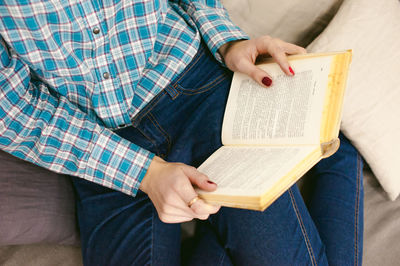 Midsection of woman reading novel on sofa